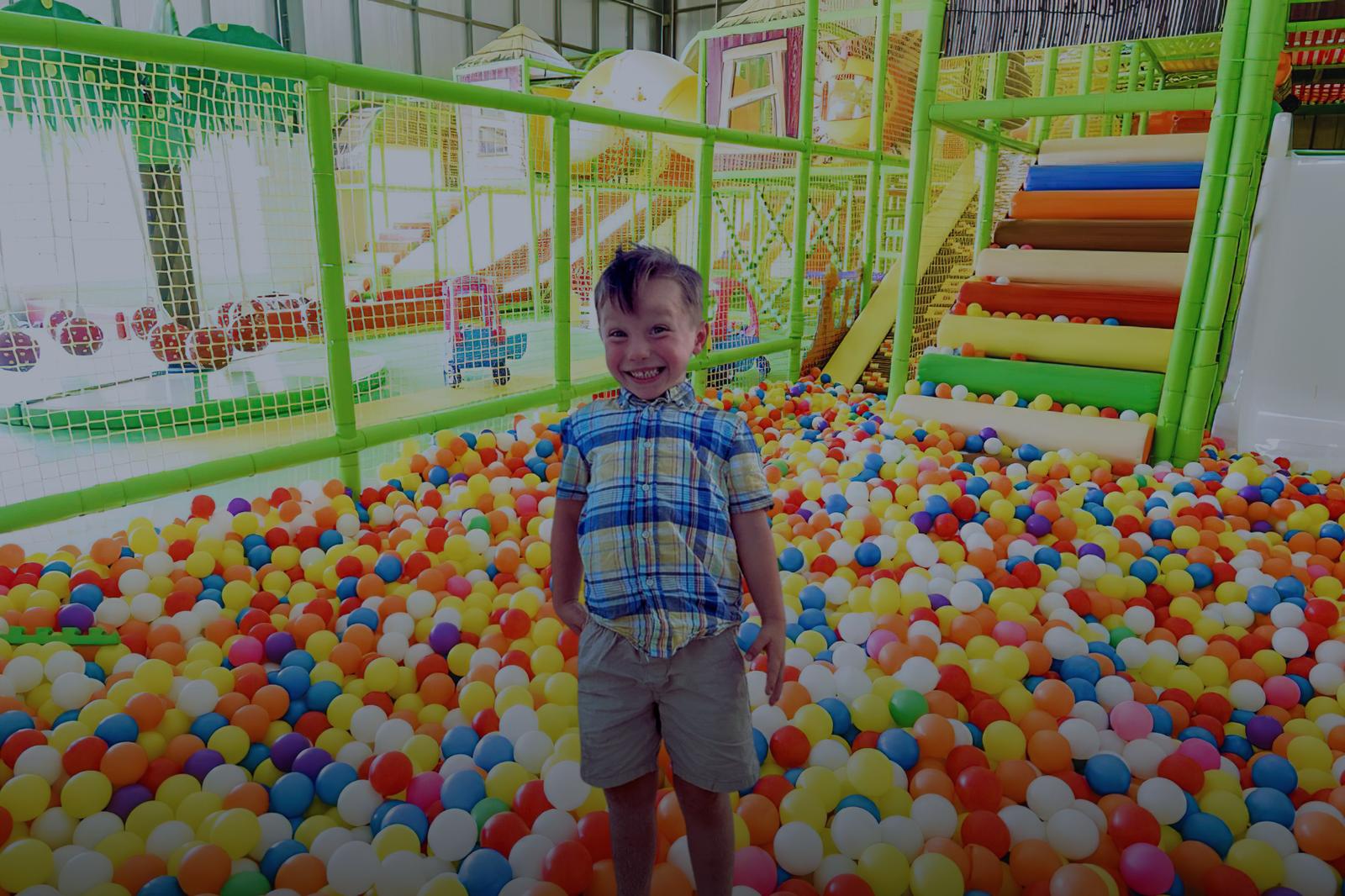 A young child standing in a colorful ball pit in the toddler zone